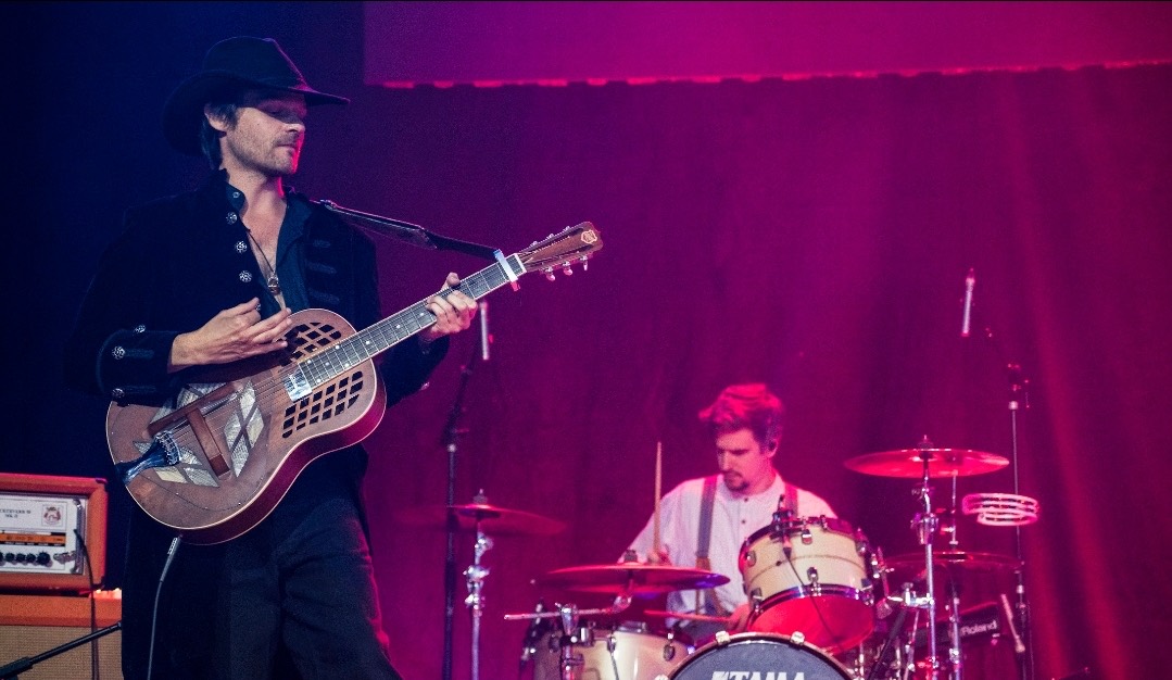 Chris Green playing a resonator guitar, drummer behind